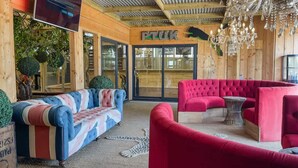 A wooden interior with a TV mounted on the wall, a chandelier, and two sofas. - Berney Lodge - Puppy Lounge Arcades Games Room (Market Rasen)