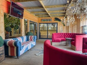 A wooden interior with a TV mounted on the wall, a chandelier, and two sofas. - Berney Lodge - Puppy Lounge Arcades Games Room (Market Rasen)