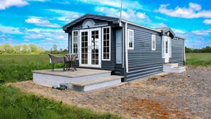 A single-story mobile home with a porch, a chair, and a small table. - Berney Lodge - Puppy Lounge Arcades Games Room (Market Rasen)