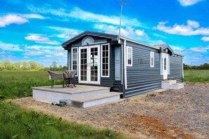 A single-story mobile home with a porch, a chair, and a small table. - Berney Lodge - Puppy Lounge Arcades Games Room (Market Rasen)