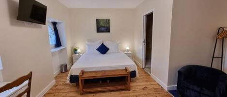 A bedroom with a bed, bedside tables, a TV, a painting, a wooden bench, and a blue sofa.