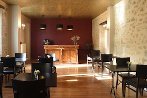 A dining area with wooden tables and chairs, a central bar area, and patterned wallpaper. - Le Rodin Bazas (BAZAS)