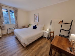 A bedroom with a bed, bedside table, lamp, chair, and a wooden table with a remote control. - Le Rodin Bazas (Bazas)