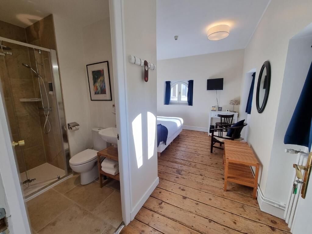 Un baño con ducha, inodoro y lavamanos; un dormitorio con cama y televisor; y un comedor con mesa y sillas.