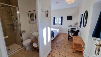 Un baño con ducha, inodoro y lavamanos; un dormitorio con cama y televisor; y un comedor con mesa y sillas.