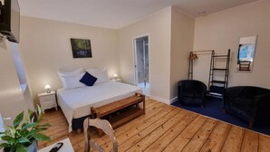 A room with a bed, bedside table, lamp, chair, wooden floor, and a TV.