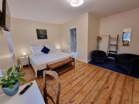 A room with a bed, bedside table, lamp, chair, wooden floor, and a TV.. Le Rodin Bazas