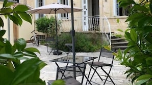 An outdoor patio with a table and chairs, a large umbrella, and a building in the background. - Le Rodin Bazas (Bazas)