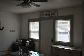 Una habitación con ventilador de techo, dos ventanas con persianas, un tocador y un cartel que dice 'love never fails'.