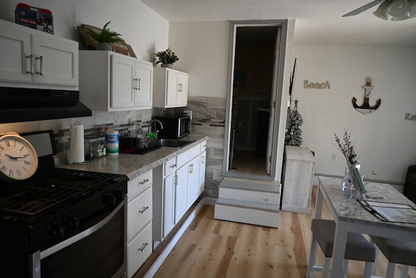 A kitchen with white cabinets, a stove, and a microwave. There is a dining area with a table and chairs.