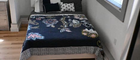 Ein Schlafzimmer mit einem Bett, Kissen, einem Fenster und einem Holzboden.