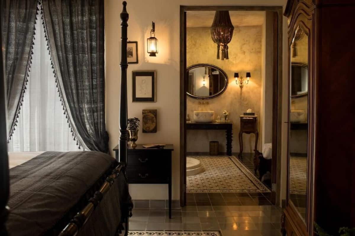 A bedroom with a bed, a nightstand, a mirror, and a wall-mounted lamp.