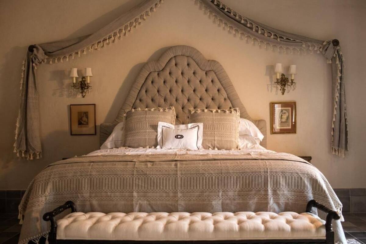 A large bed with a tufted headboard, multiple pillows, and a bench at the foot of the bed.