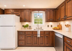 A kitchen with wooden cabinets, a white refrigerator, a window with a view, and a sink with a faucet. - Charming 1940s Cape Cod Retreat on 1 Acre - Fireplace & Large Yard (Ashland)