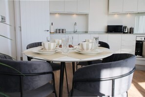 A modern kitchen with white cabinets, a dining table set with plates, glasses, and cutlery, and black chairs. - NEW Modern Apartment Free Parking Workspace (Gravesend)