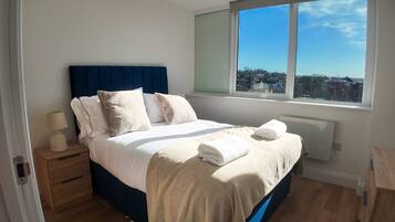 A bedroom with a bed, bedside table, lamp, and a window with a view.