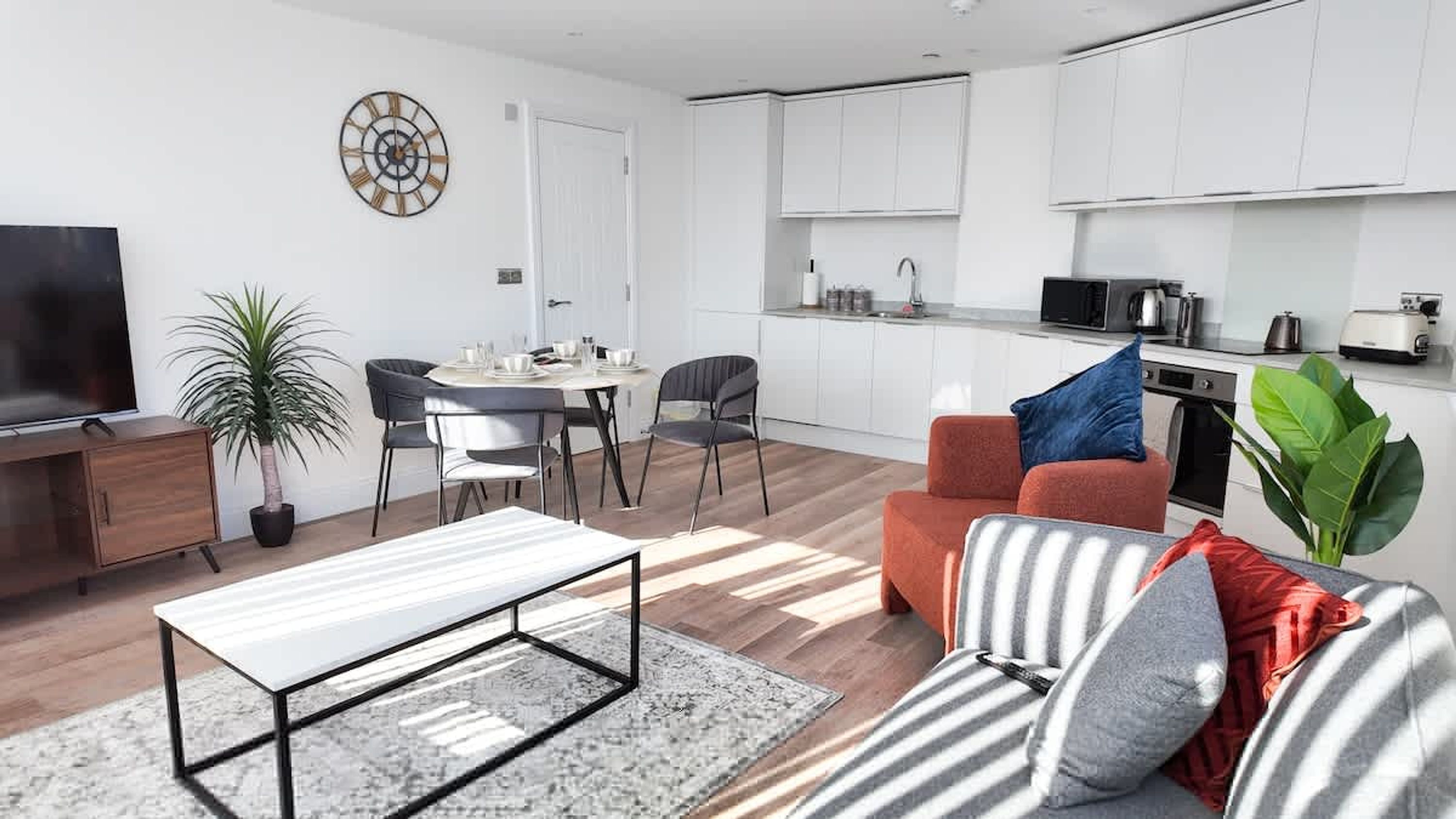 A modern living room with a TV, dining table, chairs, and a sofa with cushions.