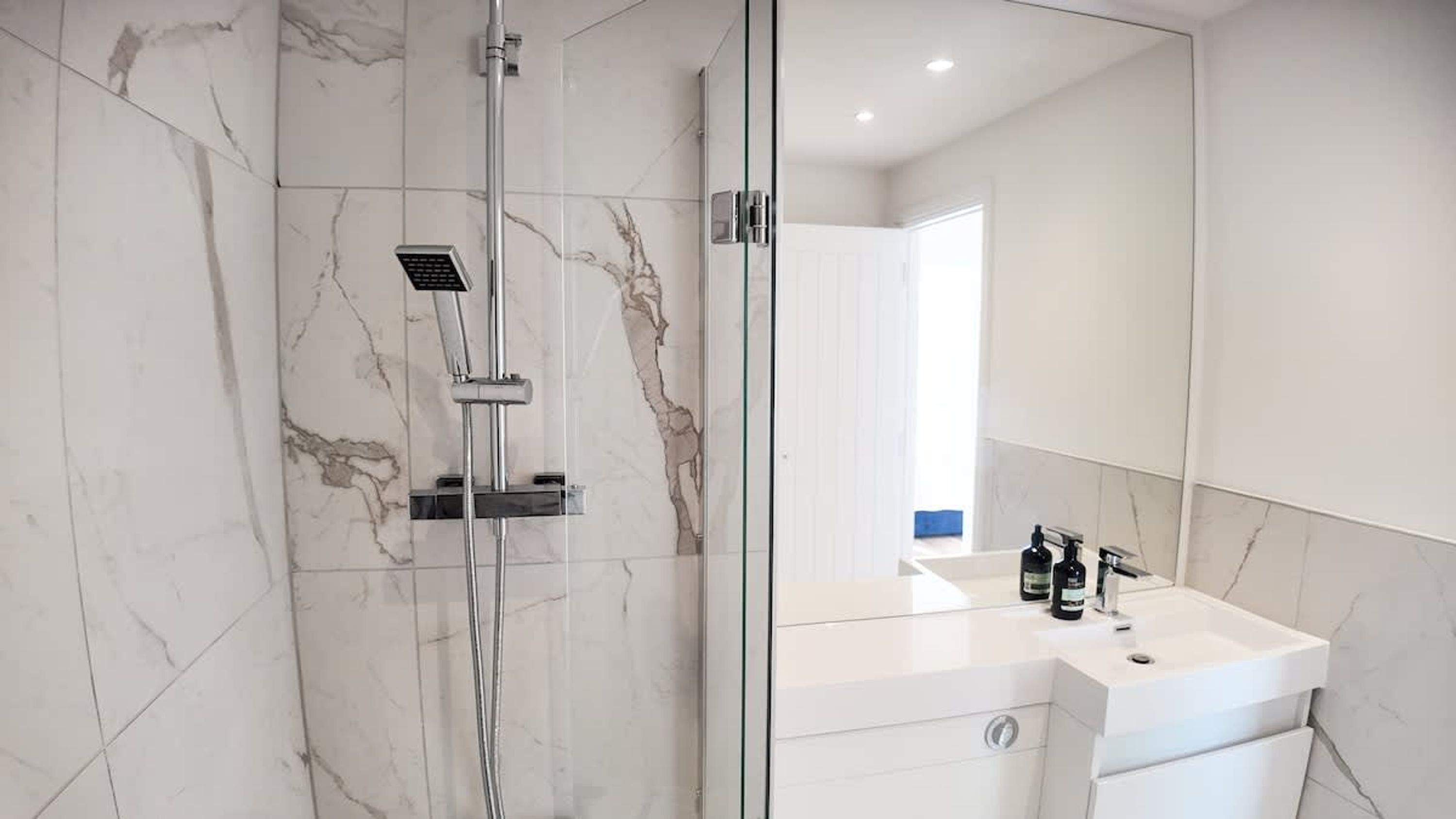 Une salle de bain moderne avec une douche à parois de verre, un lavabo blanc agrémenté d’articles de toilette et un grand miroir.
