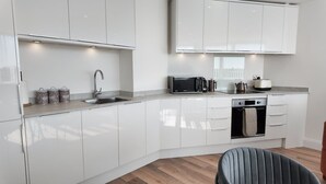 A modern kitchen with white cabinetry, a built-in oven, a microwave, and a kettle. - NEW Modern Apartment Free Parking Workspace (Gravesend)