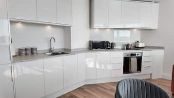 A modern kitchen with white cabinetry, a built-in oven, a microwave, and a kettle.