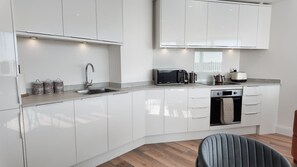 A modern kitchen with white cabinetry, a built-in oven, a microwave, and a kettle. - NEW Modern Apartment Free Parking Workspace (Gravesend)