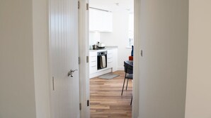 A modern kitchen with white cabinetry, a built-in oven, and a dining area with a chair. - NEW Modern Apartment Free Parking Workspace (Gravesend)