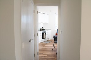 A modern kitchen with white cabinetry, a built-in oven, and a dining area with a chair. - NEW Modern Apartment Free Parking Workspace (Gravesend)