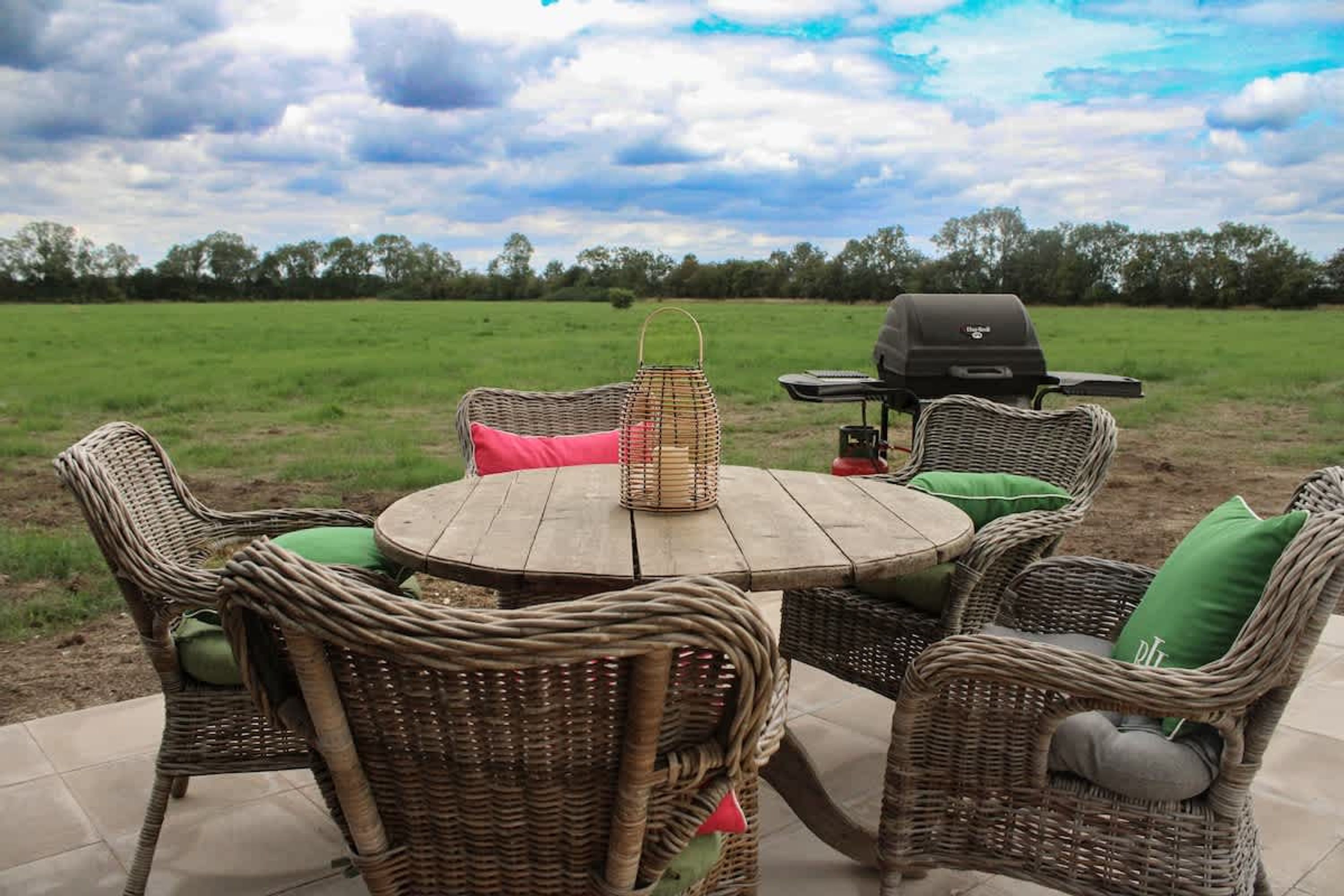 Une table ronde en bois, des chaises en osier, un barbecue et un panier.