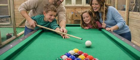 A pool table with balls, a dartboard, and cabinets in the background.