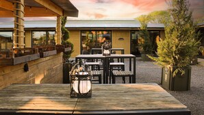 Un espace extérieur aménagé avec des tables et des chaises, une terrasse en bois et un bâtiment sur lequel est apposée une enseigne indiquant « PARKING ».