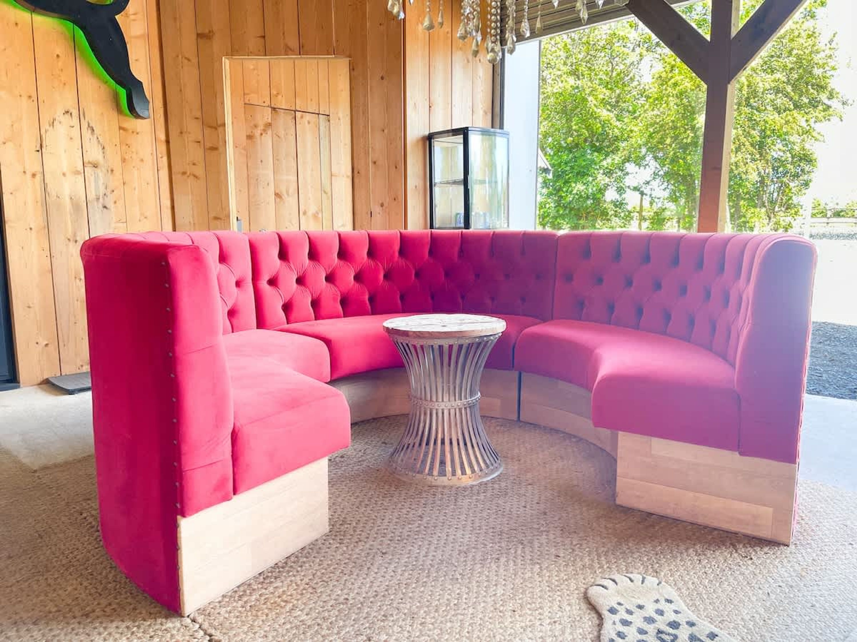 Un sofá seccional rosa con una mesa redonda en el centro, paredes de madera y vistas a árboles desde el exterior.