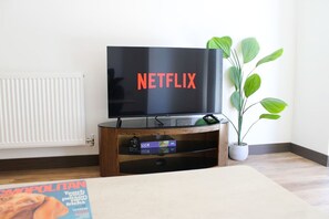 A flat-screen TV on a wooden stand with a plant beside it. - The Ivy Abode Stylish 2-bed Apartment Parking (Harlow)