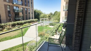 A balcony with a green chair, a small table, and a view of a garden and buildings. - The Ivy Abode Stylish 2-bed Apartment Parking (Harlow)