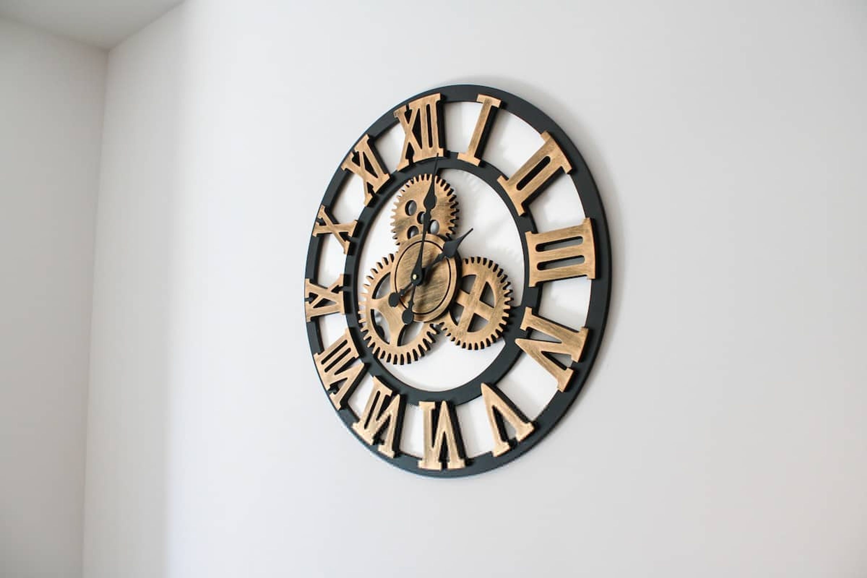 A wall-mounted clock with Roman numerals and gears.