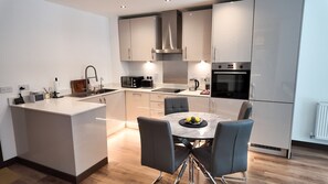 A modern kitchen with a central island, built-in appliances, and a dining area with a table and chairs. - The Ivy Abode Stylish 2-bed Apartment Parking (Harlow)