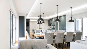 A modern dining area with grey upholstered chairs, a wooden dining table set for six, and pendant lighting. - Luxury Sea View Home With Hot Tub Sauna (Llanerchymedd)