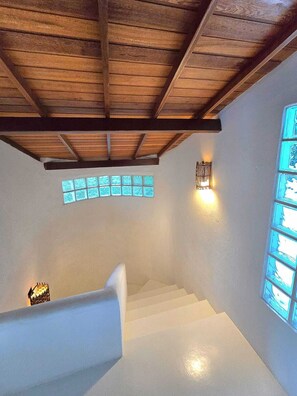 A staircase with white walls and wooden beams, a wall-mounted light fixture, and a window with a geometric pattern. - Spacious house in a large, tranquil walled garden. Close to everything. (Trancoso)