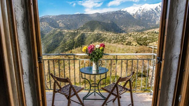 A balcony with two wooden chairs, a small round table with a vase of flowers, and a view of snow-capped mountains. - Faris Hotel - Charming Double Room Near Sparta (Sparta)