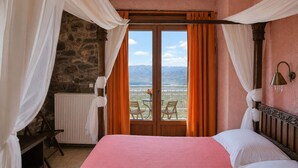 A bedroom with a bed, a view of mountains through a window, a table with chairs outside, and a stone wall. - Faris Hotel Taygetos Comfy Suite Near Sparta (Sparta)