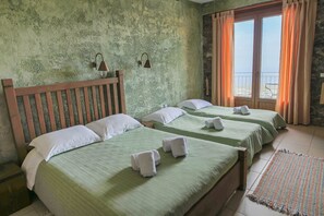 Habitación con tres camas, pared de piedra y balcón con cortinas.