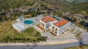 Un edificio de piedra de dos plantas con piscina, rodeado por un muro de piedra y una cerca metálica.