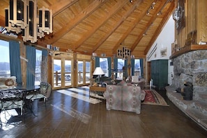 Eine geräumige Lodge mit hohen Holzbalken, einem Steinkamin und großen Fenstern mit Blick auf die Berge.
