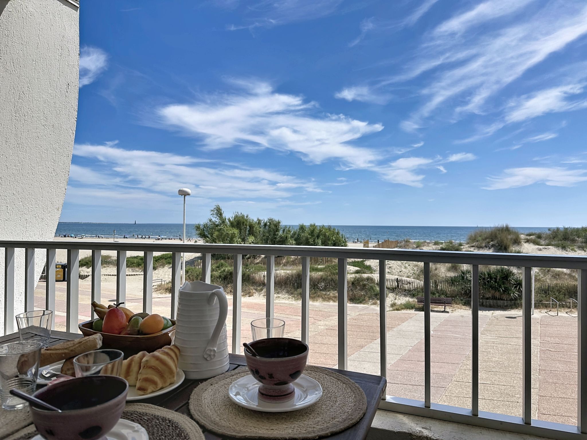 A balcony with a table set for breakfast, overlooking a beach and ocean.