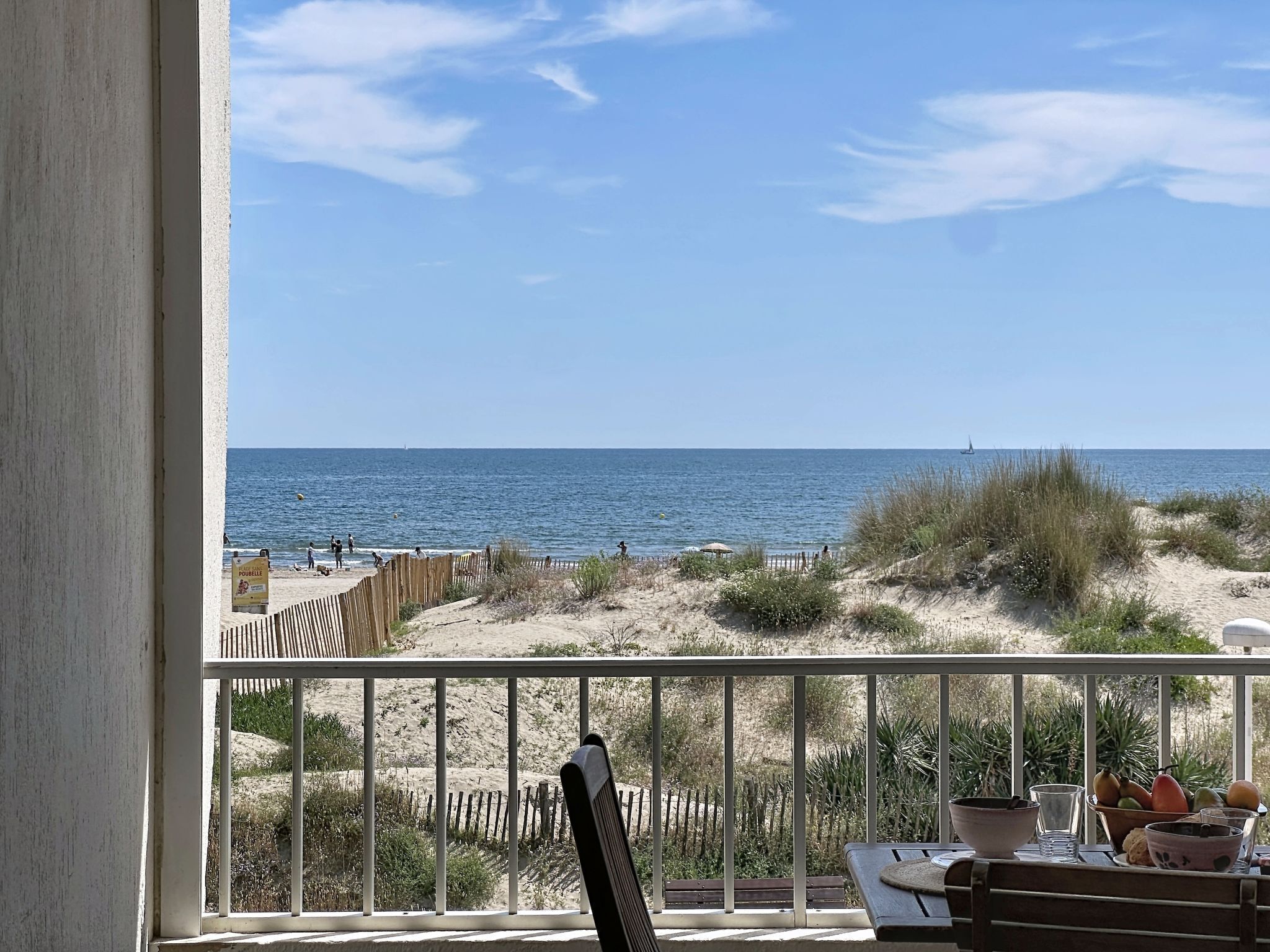 Un balcon avec vue sur la plage, une table garnie de fruits et une chaise.