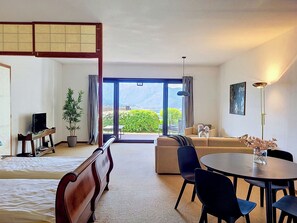 Habitació d'hotel amb llit, sofà, taula de dinar amb cadires, televisió, planta en test i vistes a la vegetació i muntanyes.