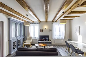 Ein modernes Wohnzimmer mit freiliegenden Holzbalken, einem Kamin, einem Fernseher und einem Essbereich.