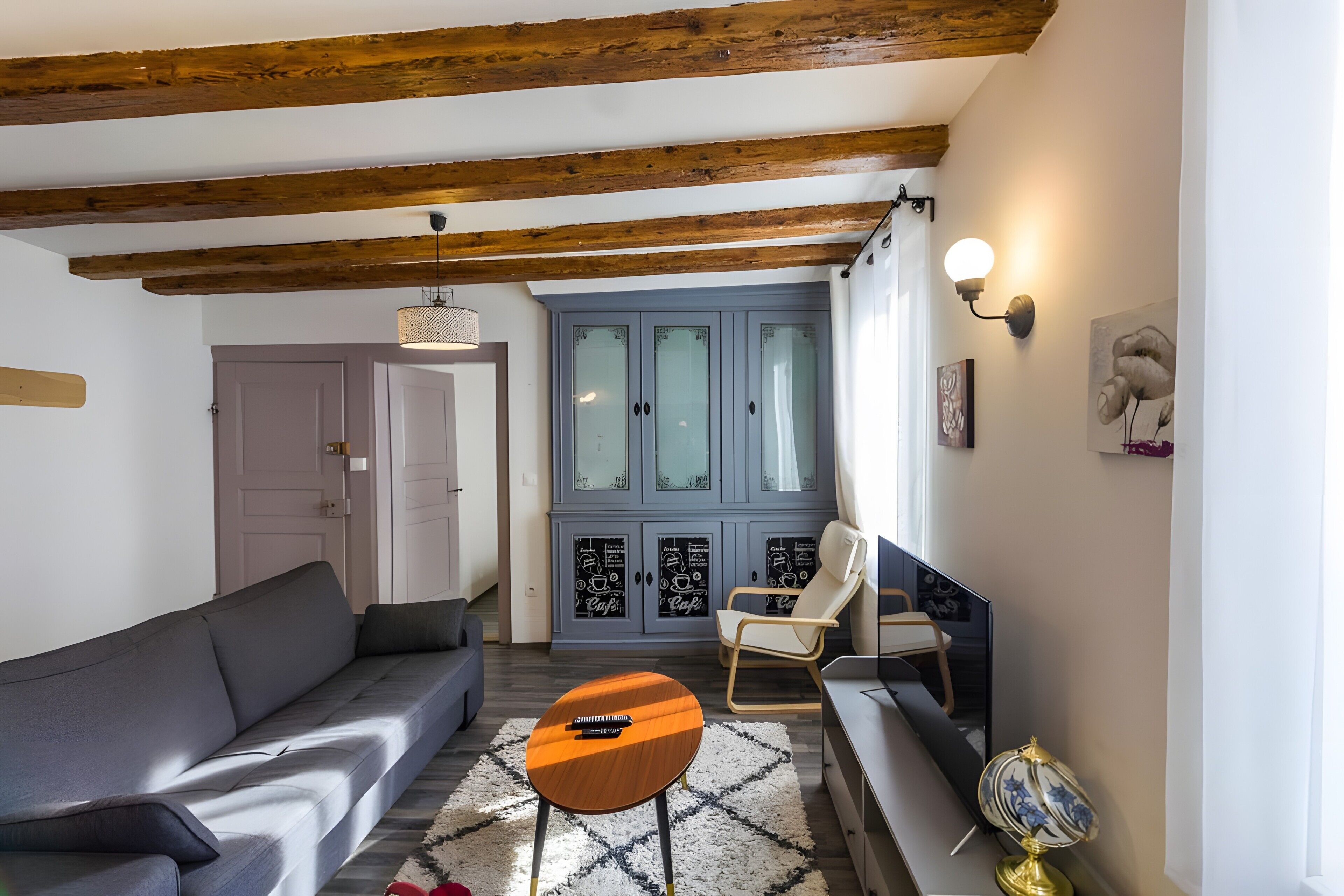 Una sala de estar con un sofá, una mesa redonda de madera, una silla y un aparador con puertas de cristal.