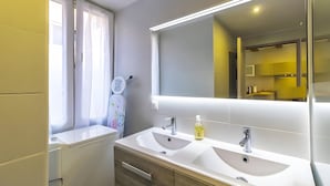 A modern bathroom with two sinks, a large mirror, and a window with curtains.