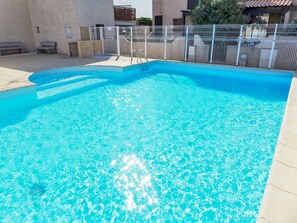 A clear blue swimming pool with a metal fence, benches, and a building in the background. - Les Villas sur la Colline by Interhome (Narbonne-Plage)