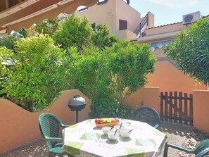 Een terras met een tafel gedekt voor twee personen, omringd door groen en een hek.